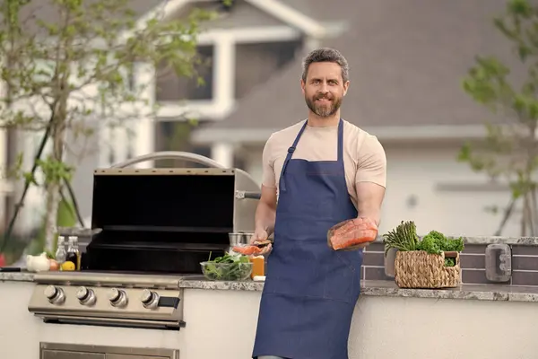 stock image chef with grilled salmon, copy space. chef man cooking grilled salmon outdoor. grilled salmon fish at man wear chef apron. photo of chef with grilled salmon.