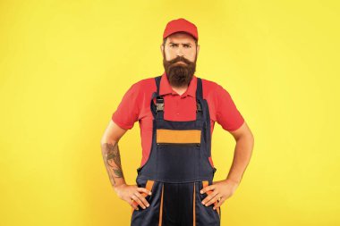 serious bearded deliveryman in work clothes on yellow background.