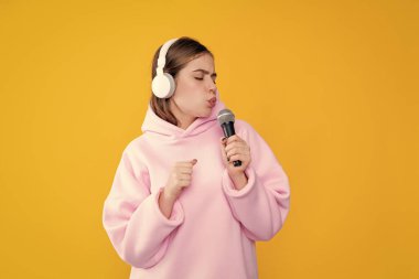 Sarı arka planda mikrofonu olan kulaklıklı komik bir genç kız..