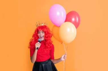 cheerful child in crown with microphone and party balloon on yellow background.
