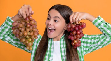 amazed teen kid with fresh grapes bunch on yellow background.