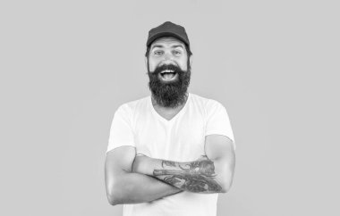 Sarıda izole edilmiş mutlu sakallı teslimatçı. Stüdyodaki sakallı teslimatçı. Arka plandaki sakallı teslimatçı. Sakallı teslimatçının şapkalı fotoğrafı..