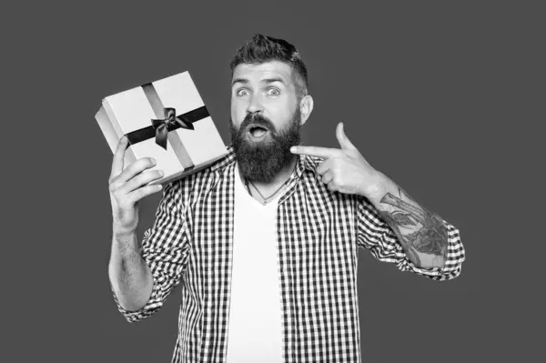 stock image mature bearded man with present box on grey background. point finger.