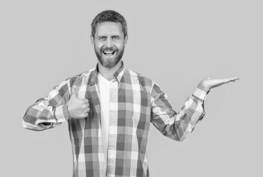 Sakallı, beyaz bir adam, sarı arka planda başparmağı yukarıda ürününü sunuyor. Stüdyoda sıradan bir beyaz adam. Beyaz adamın kareli gömlek giydiği fotoğraf. Sıradan giyinen beyaz bir adam..