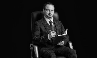 Adam ofis sandalyesinde planlama tutmuyor. Planlamacı, adamın elinde not tutuyor. Planlama yapan adamın fotoğrafı. Planlayıcısı olan adam siyah arkaplanda izole edildi.