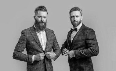 Gri arka planda, erkek giyimli yakışıklı smokinli adamlar izole edilmiş. Smokinli iki erkek giyimi. Stüdyoda erkek giyenlerin fotoğrafları. Resmi erkek giyimi giymiş zarif erkekler..