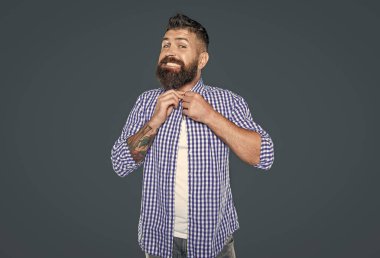 Tatmin olmuş sakallı adam gri arka planda kareli gömlek giyer..