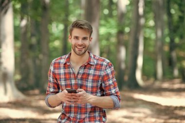 young handsome man in checkered shirt messaging on phone outdoor.