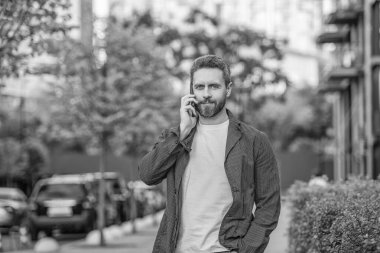 man call on mobile stands outside. photo of man call on mobile phone. man has mobile call outdoor. man having mobile call in the street.