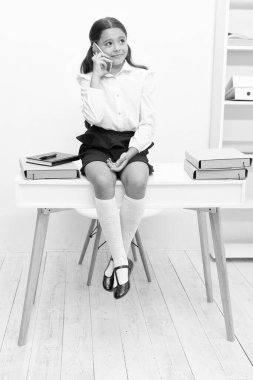 cheerful school girl has call on phone. photo of school girl has call. school girl has call in classroom. school girl has call at the desk.