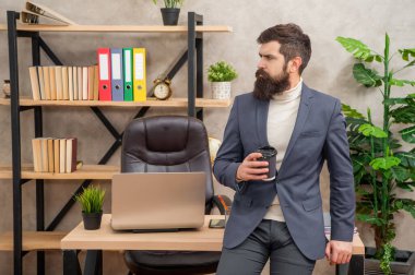 Takım elbiseli, çay ya da kahve içen ciddi bir işadamı ofis masasında oturuyor, mola veriyor..