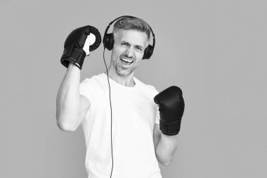 Spor eldivenli başarılı boksör kulaklık takıyor. Boks eldiveni giymiş boksör adamın fotoğrafı. Boks eldivenli erkek boksör mavi üzerine izole edilmiş. Stüdyoda boks eldivenli bir adam..