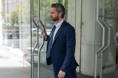 Takım elbiseli Amerikalı işadamı ofis binasını terk ediyor. CEO ofise giriyor. İş adamı. Başarılı bir iş adamı ofise giriyor. Ofis kapısında olgun bir girişimci..