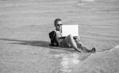 Uzaktan kumanda çalışıyor. İş adamı plajda rahatlar. Yazın dizüstü bilgisayarı olan takım elbiseli bir iş adamı. İş adamı yazın denizde iş yapmayı hayal eder. seyahat ve rahatlama. Kumsalda dinlenen bir iş adamı..