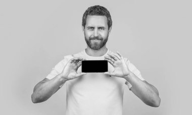 Zeki telefon uygulaması gösteren neşeli bir adam sarıda izole edilmiş. Adam arka planda akıllı telefon uygulaması gösteriyor. Stüdyoda akıllı telefon uygulaması gösteriyor. Akıllı telefon uygulaması gösteren bir adamın fotoğrafı.