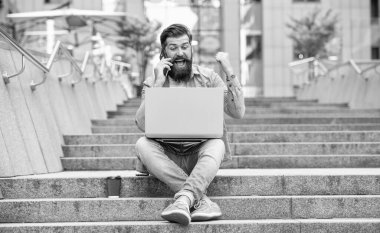 Mutlu adam cep telefonuyla konuşarak kazanma hareketi yapıyor. Bahisleri kutlayan adam merdivenlerde oturarak kazanıyor. İnternette bahis oynuyorum. Mobil bahis. Kazanmak için bahis.