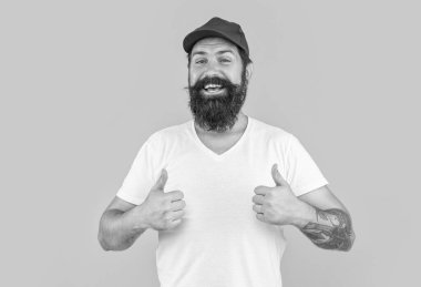 Sarı alanda izole edilmiş gülümseyen teslimatçı kurye, başparmağını kaldır. Teslimatçı kurye arka planda. Teslimatçı kurye stüdyoda. Kuryenin şapkalı fotoğrafı..