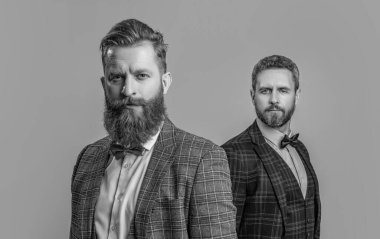 Smokinli damatlar, gri giyimli adamlar. Stüdyodaki smokinli erkekler. Smokinli erkekler arka planda. Smokinli erkeklerin resmi erkek giyimi..