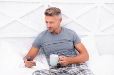 smiling man messaging in morning. man messaging in morning in bed. man messaging in morning in bedroom. photo of man messaging in morning at home.