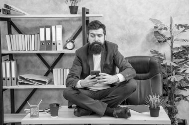 Kafası karışmış profesyonel bir adam akıllı telefondan mesaj okuyor. Ofis masasında bağdaş kurmuş oturuyor..