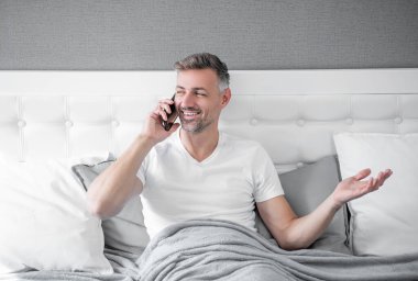 Yatakta olgun bir adam telefonda konuşuyor..