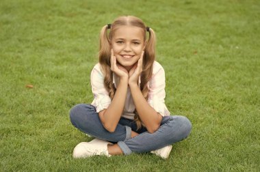 Genç kız dışarıda oturuyor. Gençliğin çocukluk tarzı. Yaz çimlerinde rahatla. Kız çimlerin üzerinde huzur içinde dinleniyor. Genç kızın mutlu çocukluğu. Yaz tatilinde parkta dinlenmek. Doğayla çevrili..