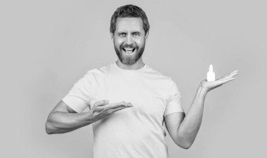 Geçmişinde burun tıbbı olan bir adam, ürünü sunuyor. Stüdyoda burun tıbbı olan bir adam. Burun tıbbı damlaları olan bir adamın fotoğrafı. Burun tıbbı olan adam sarıda izole edilmiş..