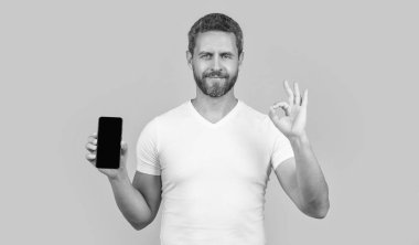 Telefon ekranı gösteren bir adam var. Tamam. Sarı arkaplanda izole edilmiş bir telefon ekranı gösteriyor. Stüdyoda telefon ekranı var. Ekranda telefon gösteren adam.