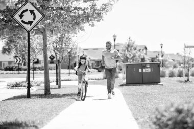 Baba oğul birlikte dolambaçlı yollarda yol alırlar. Baba-oğul gezintisi. Baba ve oğul babalığında. Baba ve oğlunun babalığı güneşli parkta bisiklet sürüyor. İki tekerlek bağlantısı.