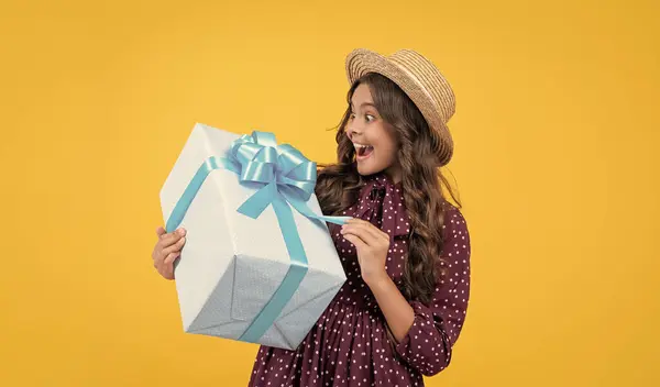 Stock image surprised teen girl with present box on yellow background.