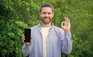 Adam akıllı telefonu açık havada sunuyor, tamam mı? Akıllı telefon ekranında fotokopi alanı sunuyor. Akıllı telefon sunan adamın fotoğrafı. Akıllı telefon sunan adam.