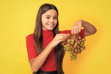 Mutlu çocuk sarı arka planda taze üzüm meyvesi tutuyor..