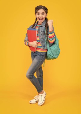 Kazanan jest yaptığı için heyecanlı bir kız. Genç kız okula geri döndü. Kitapları sarı arka planda tutan genç bir kız. Okul eğitimi.