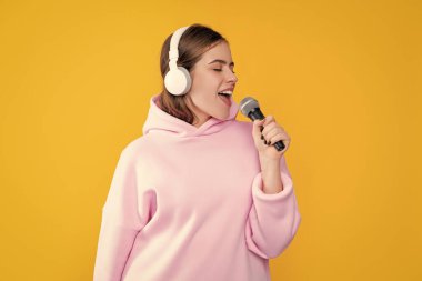 Sarı arka planda mikrofonu olan kulaklıklı mutlu genç bir kadın..