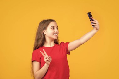 Mutlu çocuk sarı arka planda akıllı telefondan selfie çekiyor..