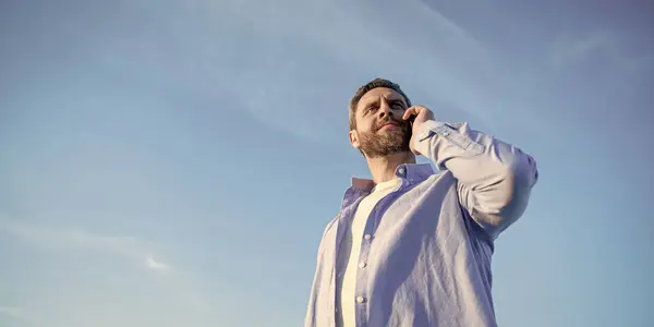 stock image communication of positive man talk on phone. man talking on smartphone. man communication talk on sky background. copy space.