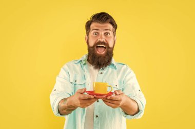 Şaşırmış sakallı adam sabah kahvesini sarı arka planda içer, kapuçino.