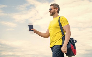 Guy traveler holding travel bag and document sky background, copy space.