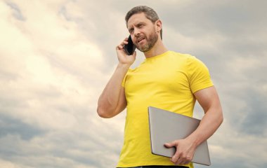 Bilgisayarlı bir adam gökyüzünde akıllı telefondan konuşuyor. modern yaşam.