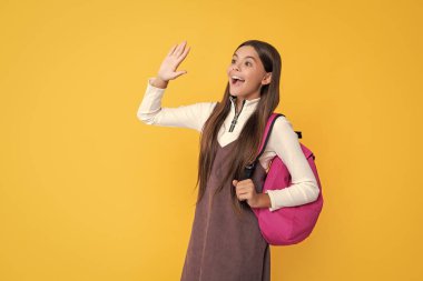 amazed child with school backpack on yellow background.