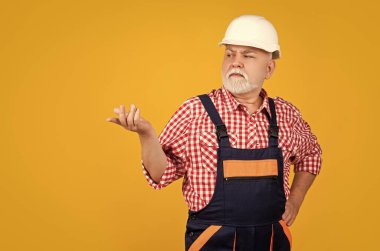 senior man builder in helmet on yellow background.