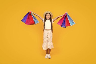 amazed teen girl with shopping bags on yellow background. full length.