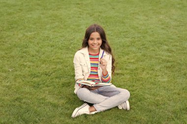 smiling teen girl making notes in notebook sitting on grass. taking notes. student make notes outdoor.