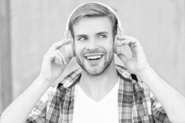 Dışarıda müzik dinleyen bir adam. Müzik dinleyen ve kareli gömlek giyen yakışıklı bir adam. Kulaklıkla müzik dinleyen bir adamın fotoğrafı. Adam açık havada müzik dinliyor..