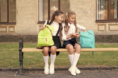 two school girls sit on bench with backpack together. sisterhood.
