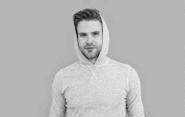 Erkek portresi. Yakışıklı adam sıradan bir kapüşonlu giyiyor. Tıraşsız yüzlü genç bir adam. Beyazların stüdyosu gri arka planda izole edilmiş..