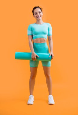cheerful sportswoman in sportswear with fitness mat in studio. fitness sportswoman in sportswear hold mat isolated on yellow background. fitness and sport.