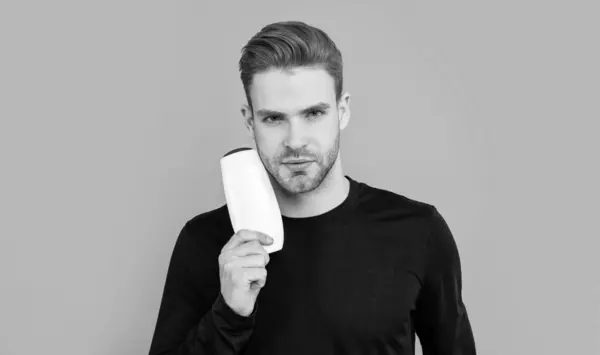 Stock image portrait of man hold unbranded cosmetics isolated on grey background. man with unbranded cosmetic in studio. unbranded cosmetic for man. handsome man hold bottle of unbranded cosmetic.