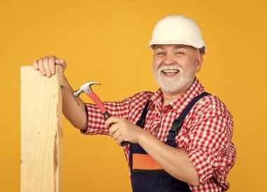 happy old aged man woodworker in helmet on yellow background.