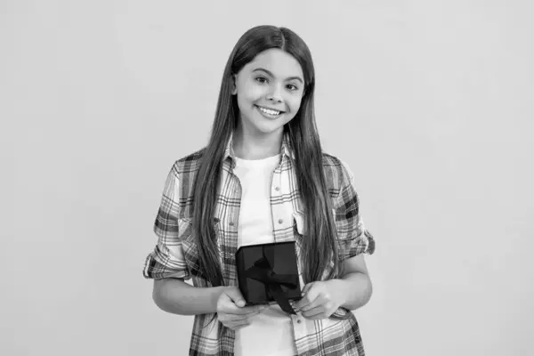 stock image smiling teen girl holding birthday present box on background. birthday teen girl posing. teen girl with birthday gift isolated on yellow. teen girl celebrating birthday with present in studio.